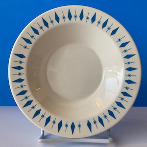 May include: A white ceramic bowl with a blue and white geometric pattern around the rim. The bowl is on a white stand.