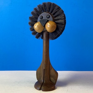 May include: A wooden lion figurine with a black bristle brush for a mane. The lion has a wooden face with gold painted eyes and a black nose.