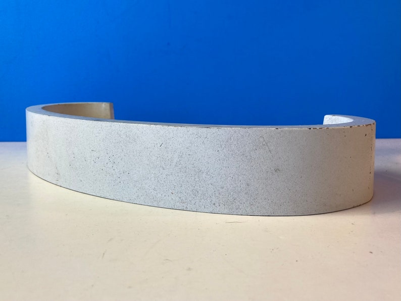 May include: A white, curved, ceramic piece with a rough, textured surface.