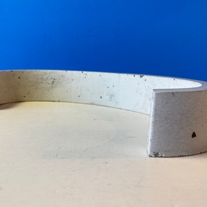 May include: A white concrete curved shelf with a rough texture. The shelf is designed to be mounted on a wall.