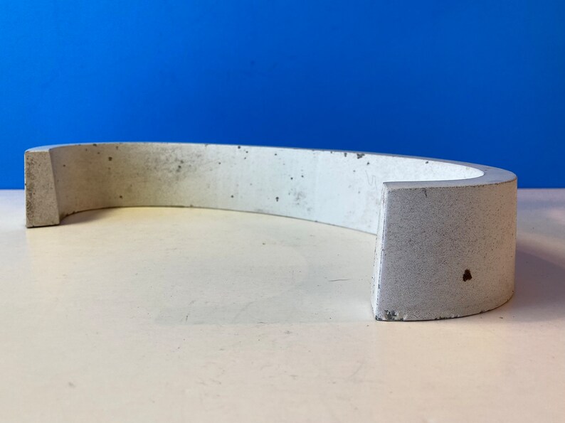 May include: A white concrete curved shelf with a rough texture. The shelf is designed to be mounted on a wall.