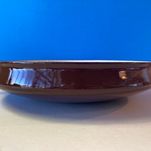 Puede incluir: Una olla de esmalte marrón con dos asas. La olla es redonda y tiene un interior blanco.