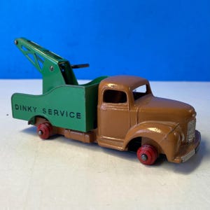 Puede incluir: Un juguete de grúa Dinky Service vintage. El camión es marrón con un brazo de remolque y una caja verdes. Las palabras "Dinky Service" están impresas en blanco en la caja verde. Las ruedas son rojas.