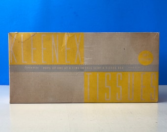 May include: A vintage Kleenex tissue box with a yellow and gray design. The box reads "Kleenex Tissues" in large yellow letters. The text "Pops up one at a time in this serv-a-tissue box" is also visible.
