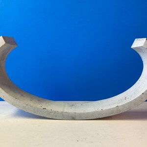 May include: A concrete half-circle sculpture with a smooth, gray surface. The sculpture is curved and has a rounded edge.