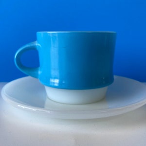 Puede incluir: Un juego de taza y platillo de café de cerámica azul y blanco. La taza tiene un cuerpo azul claro con un borde blanco y una base blanca. El platillo es blanco.