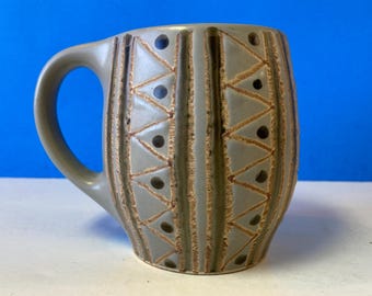 May include: A gray ceramic mug with a geometric pattern of triangles and dots. The mug has a brown handle.