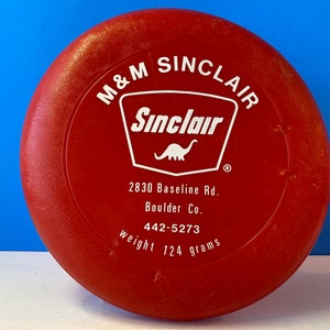 May include: Red plastic flying disc with a white Sinclair logo, a dinosaur, and the text "M&M Sinclair", "2830 Baseline Rd.", "Boulder Co.", "442-5273", and "weight 124 grams".