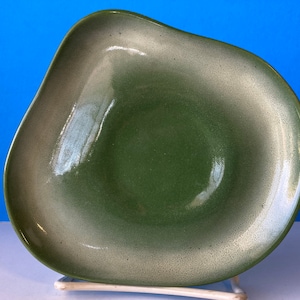 Puede incluir: Un cuenco de cerámica verde y blanco con una forma ondulada y orgánica. El cuenco tiene un esmalte moteado y un acabado brillante.