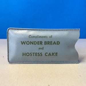 May include: A light blue, rectangular promotional item with the text "Compliments of WONDER BREAD and HOSTESS CAKE" in green. The item has a stitched border and a curved edge on one side.