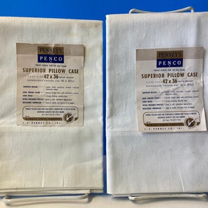 May include: Two white Penney's Penco Superior Pillow Cases, each with a label. The labels read "Superior Pillow Case" and list the case size as 42 x 36 inches. The pillowcases are folded and stacked on a white metal rack.