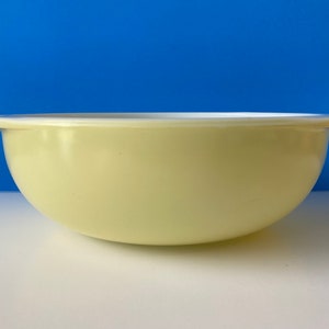 Może przedstawiać: Ceramiczna miska do mieszania w jasnożółtym kolorze z białym rantem. Miska ma zaokrąglony kształt i lekko rozszerzający się brzeg.