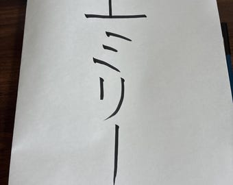 以下が含まれることがあります： 白い紙に日本語の文字と英語の名前「Emily」が黒インクで書かれています。日本語の文字は英語の名前の上に縦に並んでいます。