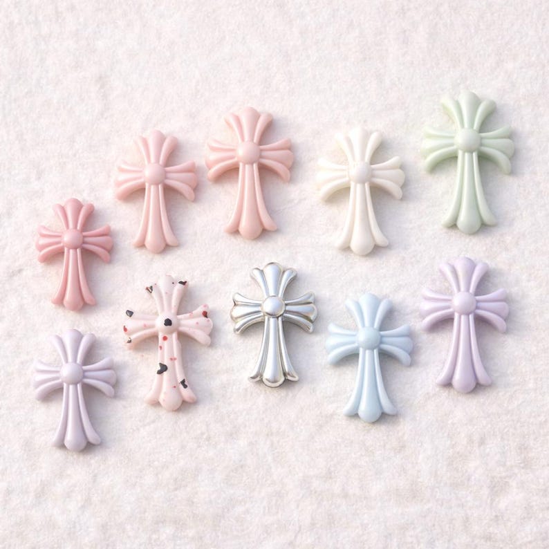 May include: A collection of decorative cross charms in various pastel colors, including pink, white, and lavender. One cross has a silver finish, and another has a speckled design. These charms are suitable for jewelry making or craft projects.