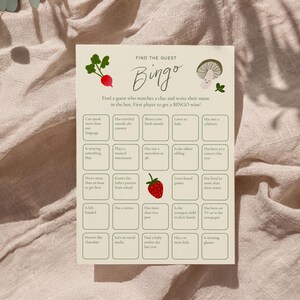 May include: A beige Bingo game card with a radish and mushroom illustration. The card has a grid of boxes with prompts like "Speaks more than one language" and "Loves to bake". The title "Find the Guest Bingo" is at the top.