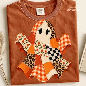 Puede incluir: Una camiseta de color óxido con un gráfico central de un fantasma compuesto por varios patrones de patchwork, incluyendo cuadros vichy naranjas, estampado de leopardo, cuadros negros y blancos y motivos florales rojos sobre fondo crema.