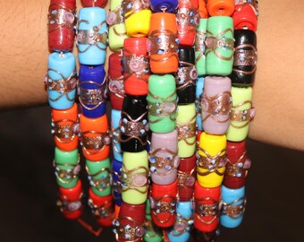 May include: A stack of colorful beaded bracelets. The bracelets feature cylindrical beads in various colors, including red, blue, yellow, and green. Each bead is adorned with a decorative metal band. The bracelets are strung together with a thin, orange string.