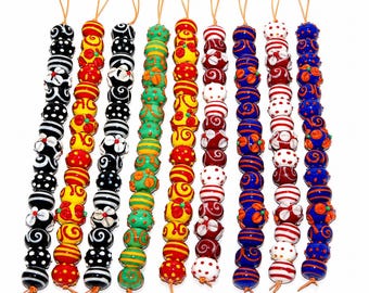 May include: Nine vertical strands of decorative glass beads, each featuring distinct patterns including stripes, dots, and floral motifs in vibrant colors like red, yellow, blue, green, black, and white, finished with a small loop at the top.