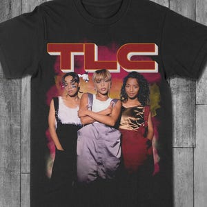 May include: Black t-shirt featuring a graphic of the music group TLC. The image shows the group members in a vintage style. The word "TLC" is printed in a red and white 3D font across the top of the image.