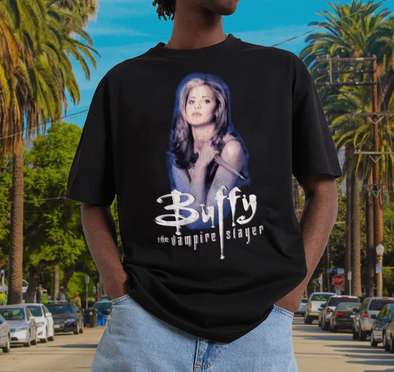 May include: Black t-shirt featuring a graphic of Buffy the Vampire Slayer. The design includes a portrait of the character and the show's logo in white. The shirt is a classic crew neck style.