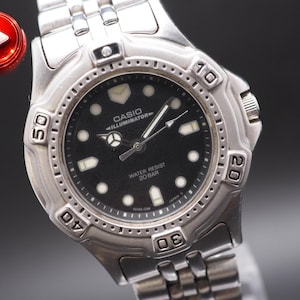 May include: A silver Casio Illuminator watch with a black dial. The watch features white hour markers, a date display, and a stainless steel band. The watch face displays the text "WATER RESIST 20 BAR".