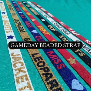 May include: A collection of beaded straps in various colors, each displaying team names and phrases like "Jackets," "Leopards," and "Fight On." The straps are adorned with stars and hearts, and the text "GAMEDAY BEADED STRAP" is visible.