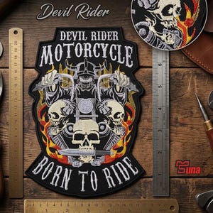 May include: A large embroidered patch featuring a skull wearing a helmet, flames, and the text 'DEVIL RIDER MOTORCYCLE BORN TO RIDE'. It measures 11.5 x 7.6 inches. A smaller circular patch with a skull and flames is also shown next to a metal ruler.