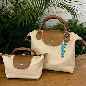 May include: Two beige canvas handbags with brown leather details. The larger bag has a top handle and a small charm that says "Krien". The bags have a flap closure with the text "ZERE & BAGS FRANCE".