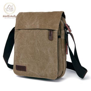 May include: A brown canvas messenger bag with a flap closure and a long, adjustable shoulder strap. The bag features a small leather accent and a rectangular patch with text. The bag is designed for carrying items.