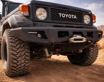 May include: A black Toyota off-road vehicle with large, rugged tires is parked on a sandy surface. The front of the vehicle features a black grill with the Toyota logo, round headlights, and a heavy-duty bumper with a winch.