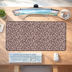 May include: A rectangular desk mat with a leopard print pattern in shades of brown and tan. The mat is surrounded by a black border. A white keyboard and mouse are visible below the mat, and a curved monitor is above.