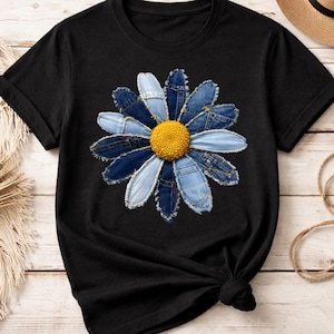 May include: Black t-shirt featuring a denim flower design. The flower has blue denim petals and a yellow center. The t-shirt has short sleeves and a crew neck.