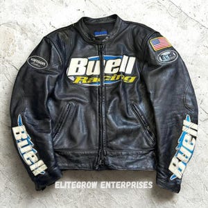 May include: Black leather motorcycle jacket with the "Buell Racing" logo in white, yellow, and blue across the chest. Features an American flag patch on the right sleeve and "Buell" lettering on the left sleeve. Includes a zipper closure and multiple pockets.