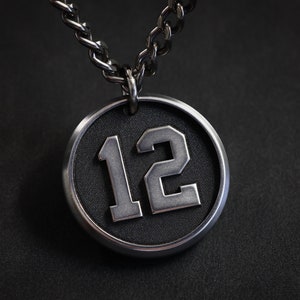 May include: A silver chain necklace with a round pendant featuring the number 12 in a white, raised font on a black background.