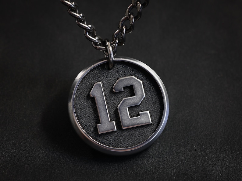 May include: A silver chain necklace with a round pendant featuring the number 12 in a white, raised font on a black background.