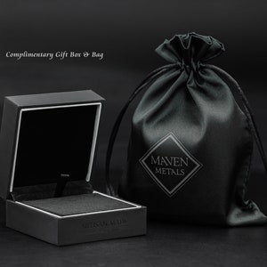 May include: A black square gift box with a white interior and the text "Artisan Made" on the bottom. The box is open and next to a black drawstring bag with the text "Maven Metals" in white.