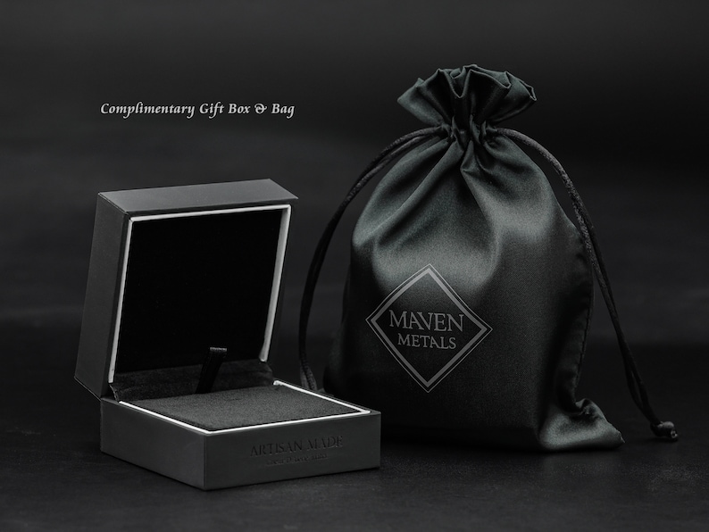 May include: A black square gift box with a white interior and the text "Artisan Made" on the bottom. The box is open and next to a black drawstring bag with the text "Maven Metals" in white.