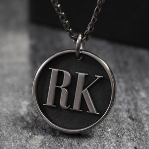 May include: A silver chain necklace with a round pendant featuring the initials "RK" in raised lettering on a black background.