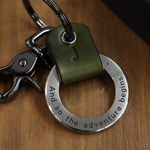 May include: A green leather keychain with a silver ring and a silver clasp. The ring has the text "And so the adventure begins" engraved on it.