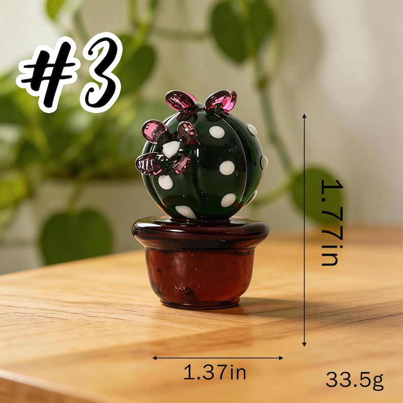 May include: A dark green glass cactus figurine with white polka dots and pink accents, set in a brown pot. The figurine is 1.77 inches tall and 1.37 inches wide, weighing 33.5 grams. The image includes the text "#3".