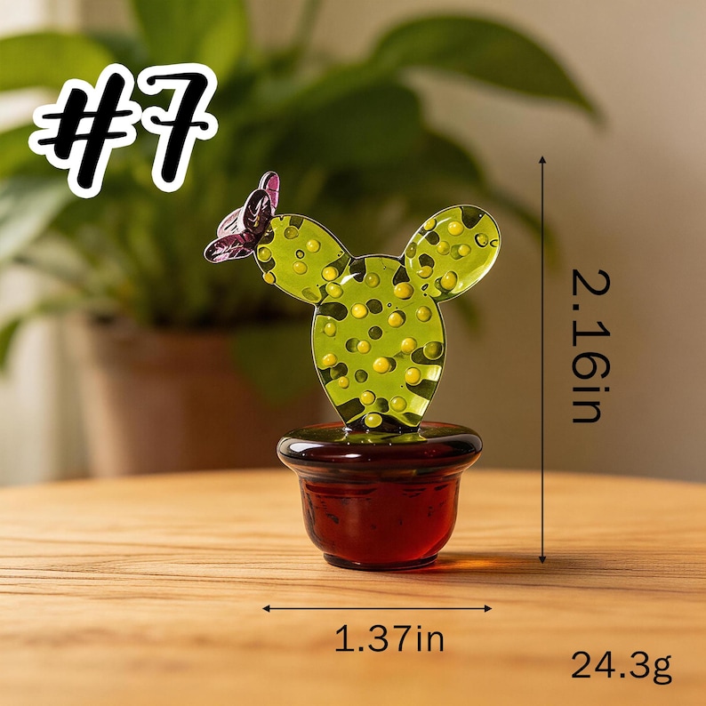 May include: A glass cactus sculpture with a butterfly accent. The cactus is green with yellow dots and sits in a red pot. It measures 2.16 inches tall and 1.37 inches wide, weighing 24.3g. The text "#7" is in the upper left corner.