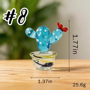 May include: A small, turquoise glass cactus with white polka dots and a red flower, displayed in a clear glass pot with black, yellow, and white accents. The cactus is 1.77 inches tall and 1.37 inches wide, weighing 25.6 grams. The image includes the text "#8".