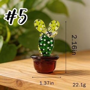 May include: A glass cactus figurine with a green body and yellow spotted leaves, set in a brown pot. The figurine is 2.16 inches tall and 1.37 inches wide, weighing 22.1 grams. The number "#5" is in the upper left corner.