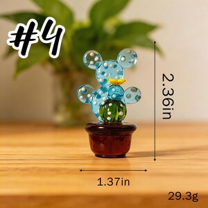 May include: A glass cactus figurine in a brown pot. The blue cactus has white polka dots and a yellow flower. It measures 2.36 inches tall and 1.37 inches wide. The figurine weighs 29.3 grams. The text "#4" is in the upper left corner.