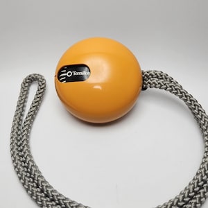 May include: An orange, spherical object with the text "Terraillon" on its surface, connected to a gray and white braided rope. The object is centered against a white background.