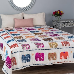 May include: White bedspread with a repeating pattern of colorful elephants. The elephants are in shades of blue, orange, pink, purple, and brown. The bedspread is on a bed with white pillows and a pink bolster pillow.