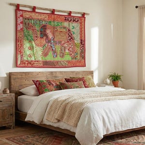 Peut inclure: Chambre avec lit en bois, literie blanche et plaid en tricot beige. Une tapisserie colorée avec un motif d'éléphant est accrochée au-dessus du lit. Une table de chevet en bois avec une lampe et une plante en pot sont à gauche.