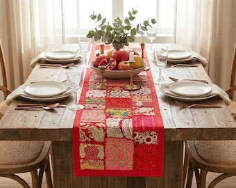 Può includere: Un tavolo da pranzo rustico in legno, apparecchiato per un pasto. Il tavolo è adornato con piatti bianchi, posate e un runner patchwork rosso. Una ciotola di frutta e verde aggiunge un tocco decorativo.