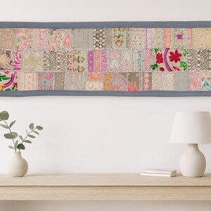 May include: A rectangular patchwork textile with a grey border. The textile is made up of many fabric squares in different colours and patterns, including floral and geometric designs. The colour palette includes pink, green, and grey.