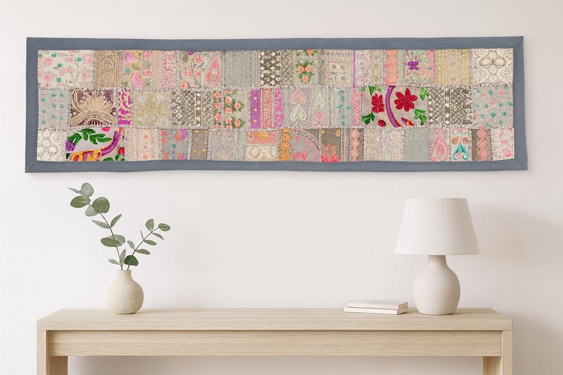 May include: A rectangular patchwork textile with a grey border. The textile is made up of many fabric squares in different colours and patterns, including floral and geometric designs. The colour palette includes pink, green, and grey.
